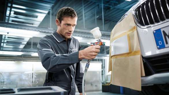 A varnisher spraying the front of a BMW. A varnisher spraying the front of a BMW.
