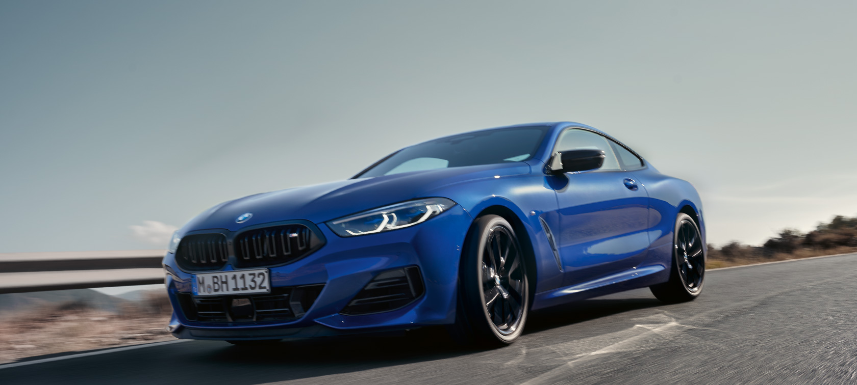 BMW 8 Series Coupé G15 LCI Facelift 2022 BMW M850i xDrive M Portimao blue metallic front view low-angle shot driving on country road in with hills in the background BMW 8 Series Coupé G15 LCI Facelift 2022 BMW M850i xDrive M Portimao Blue metallic front view low-angle shot driving on country road in with hills in the background
