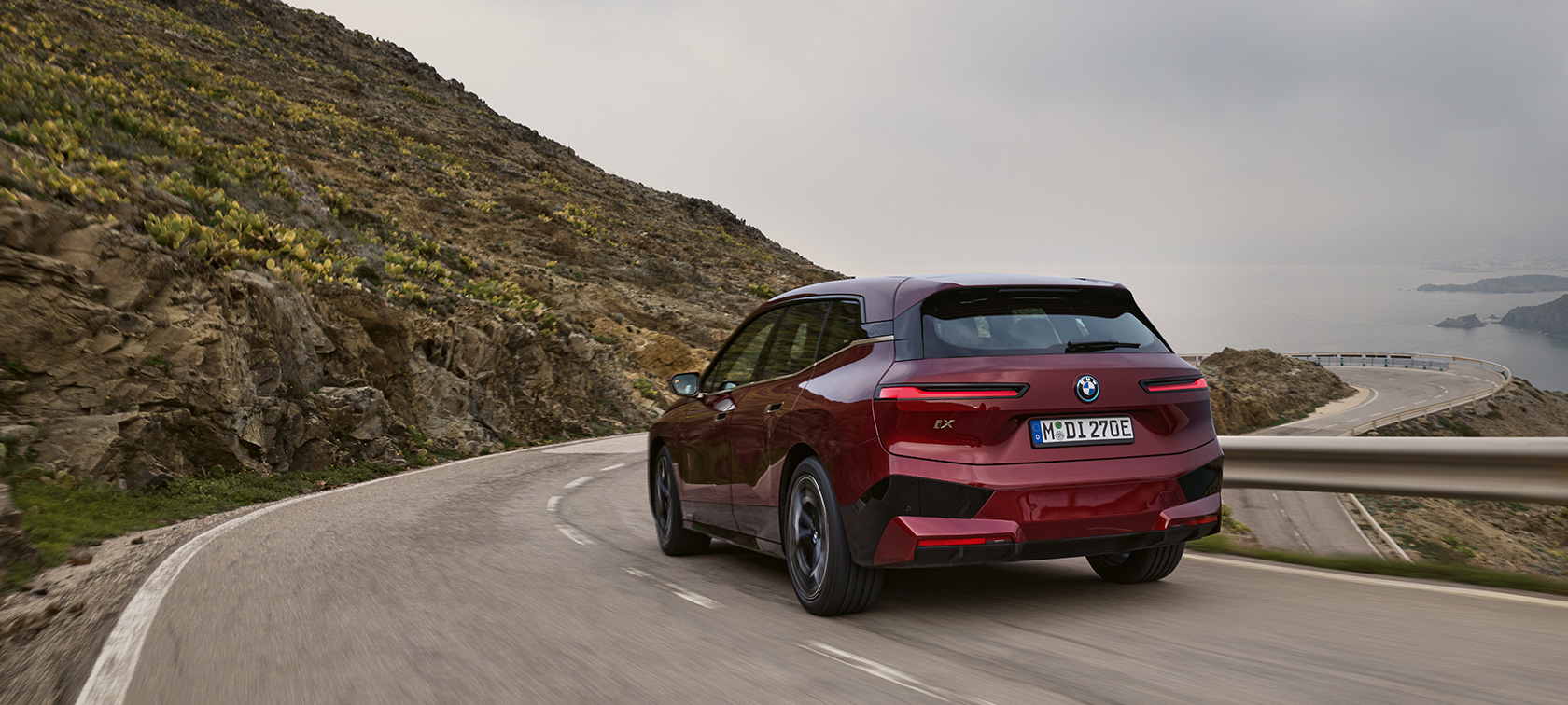 BMW iX i20 2021 electric SUV BMW iX xDrive50 driving on coastal road BMW iX i20 2021 electric SUV BMW iX xDrive50 Aventurin Red rear view driving on coastal road