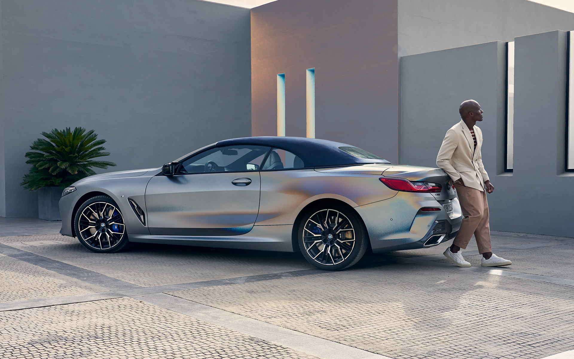 BMW M850i xDrive Convertible G14 LCI Facelift 2022 BMW Individual Frozen Pure Grey metallic three-quarter rear view with male model leaning against vehicle