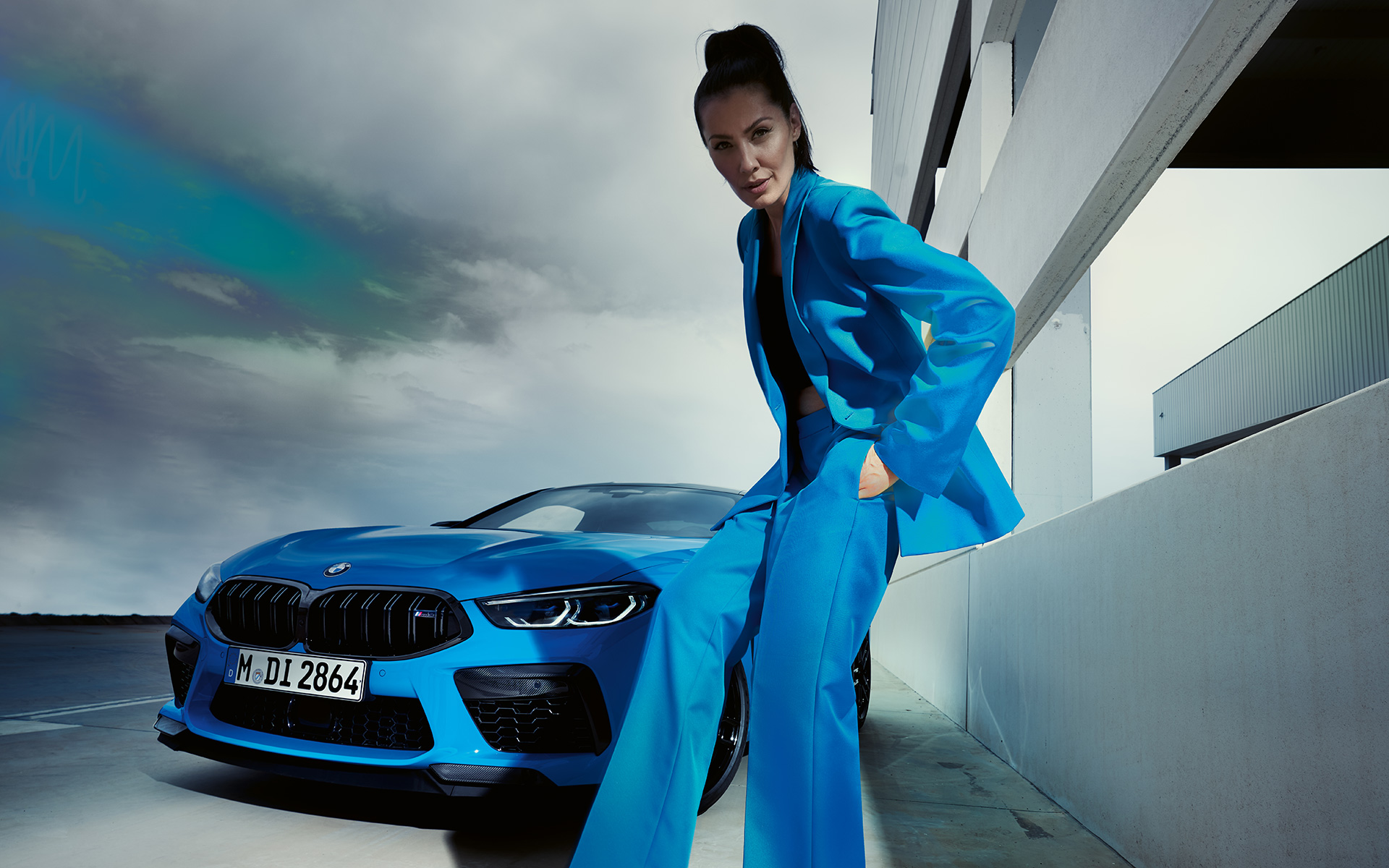 BMW M8 Competition Coupé F92 LCI Facelift 2022 Daytona Beach blue uni three-quarter front view with a female model in blue trouser suit