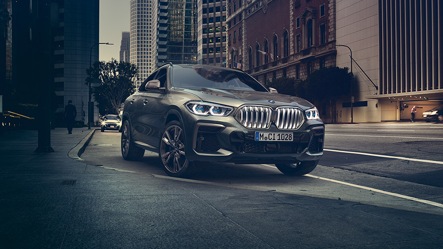 BMW X6 M50i in three-quarter front perspective standing in front of an urban setting G06 2018 SUV