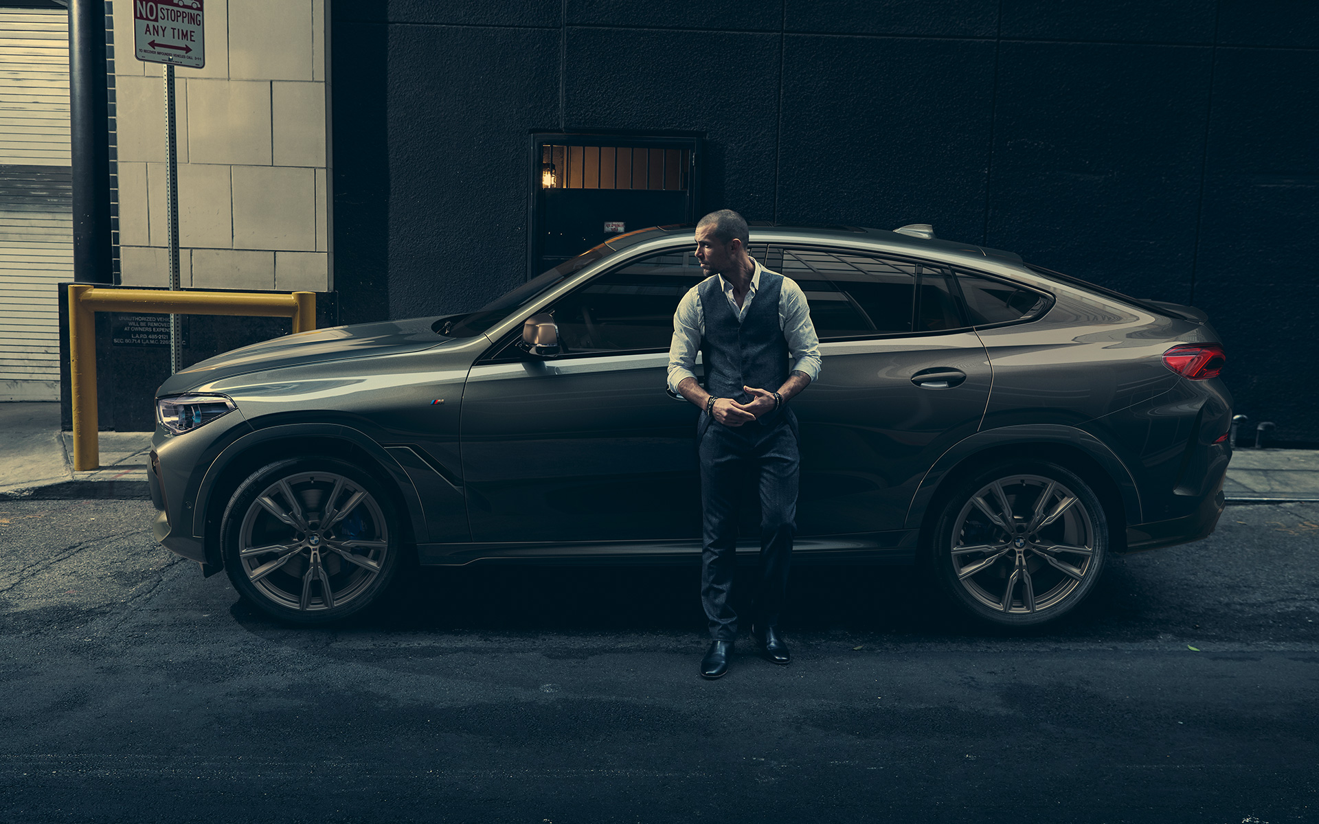 Man leaning on BMW X6 M50i in lateral perspective in front of an urban setting G06 2018 SUV