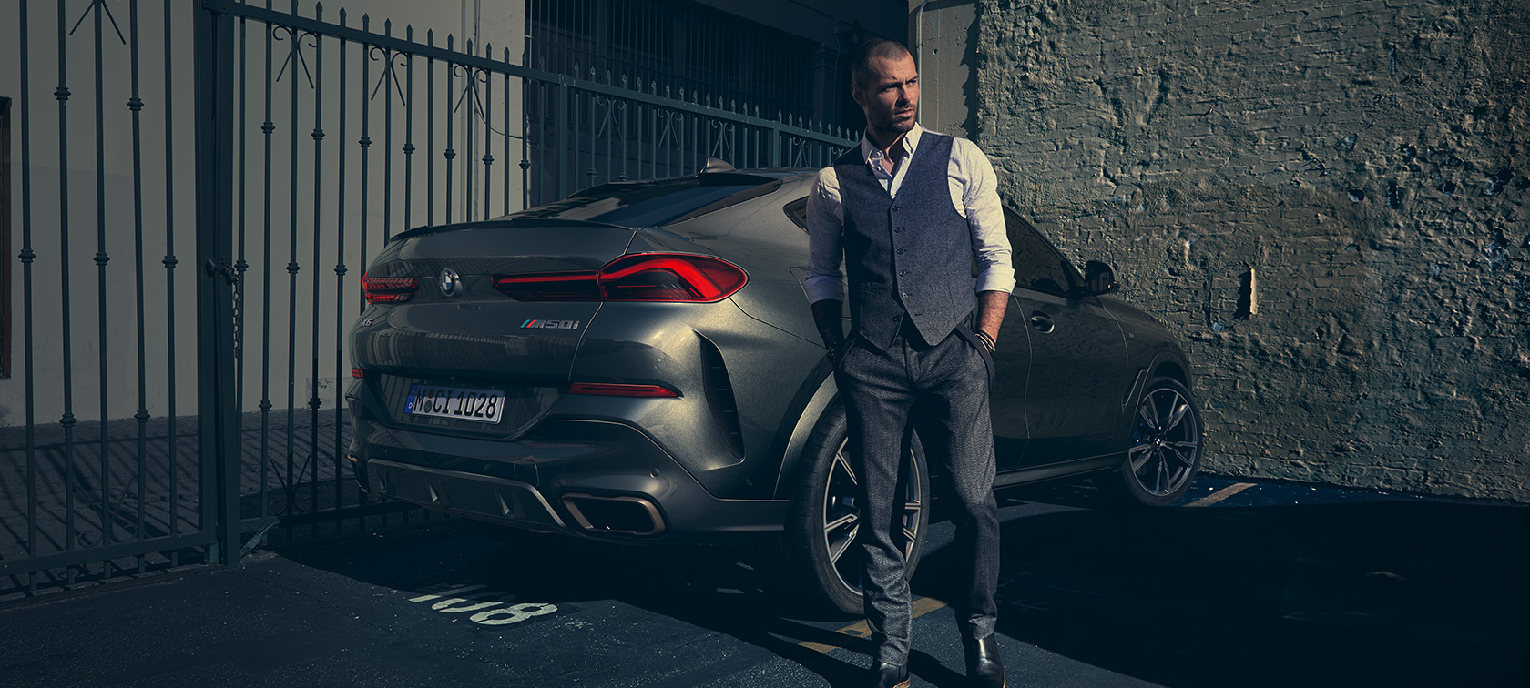Man standing next to BMW X6 M50i G06 2018 SUV in three-quarter rear view