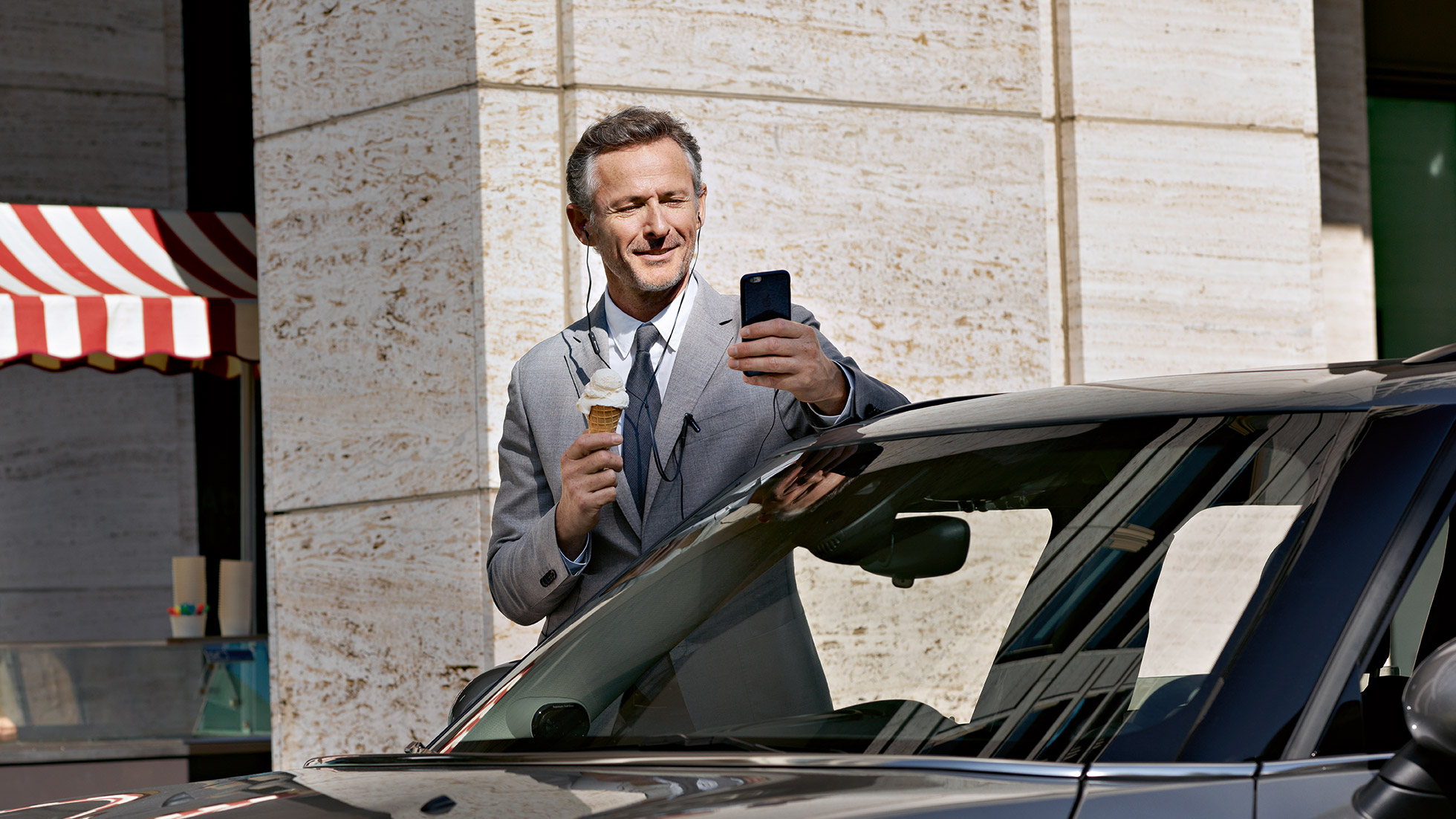 BMW Corporate Aftersales, control finances BMW Corporate Aftersales: Man eats ice cream and controls his finances via smartphone