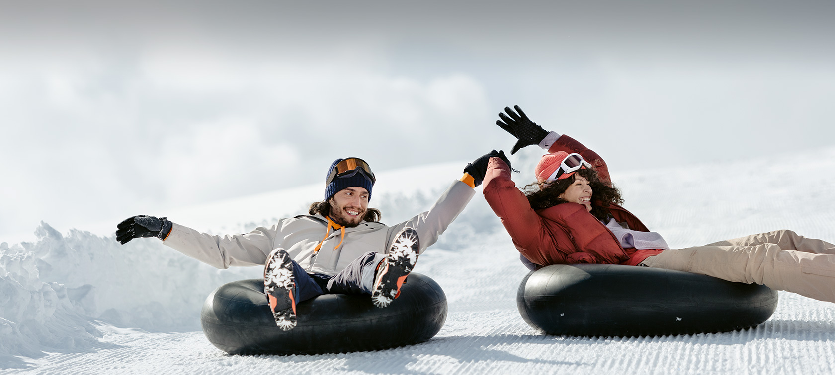 Woman and man laughing on toboggan tyres in snow 