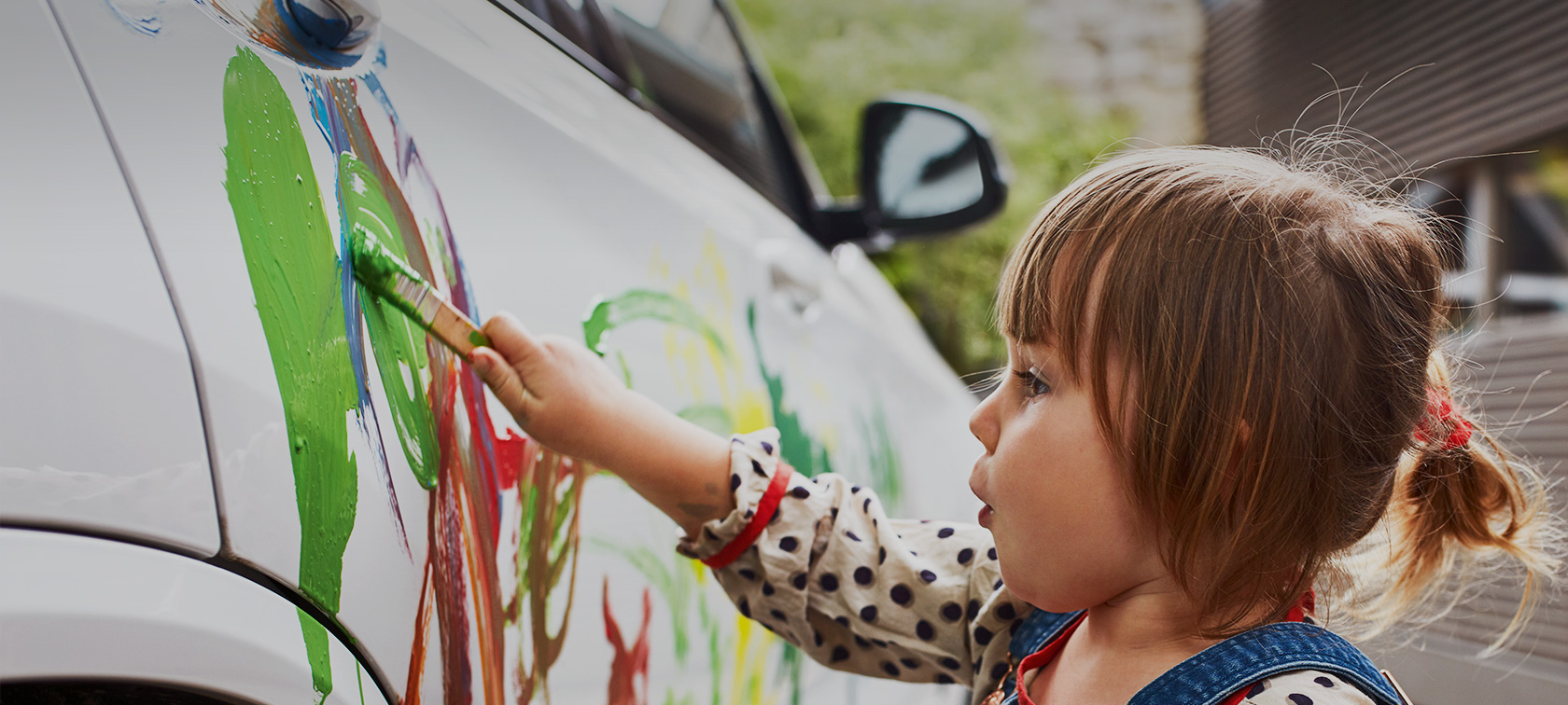 A little girl is painting a white BMW with colour.