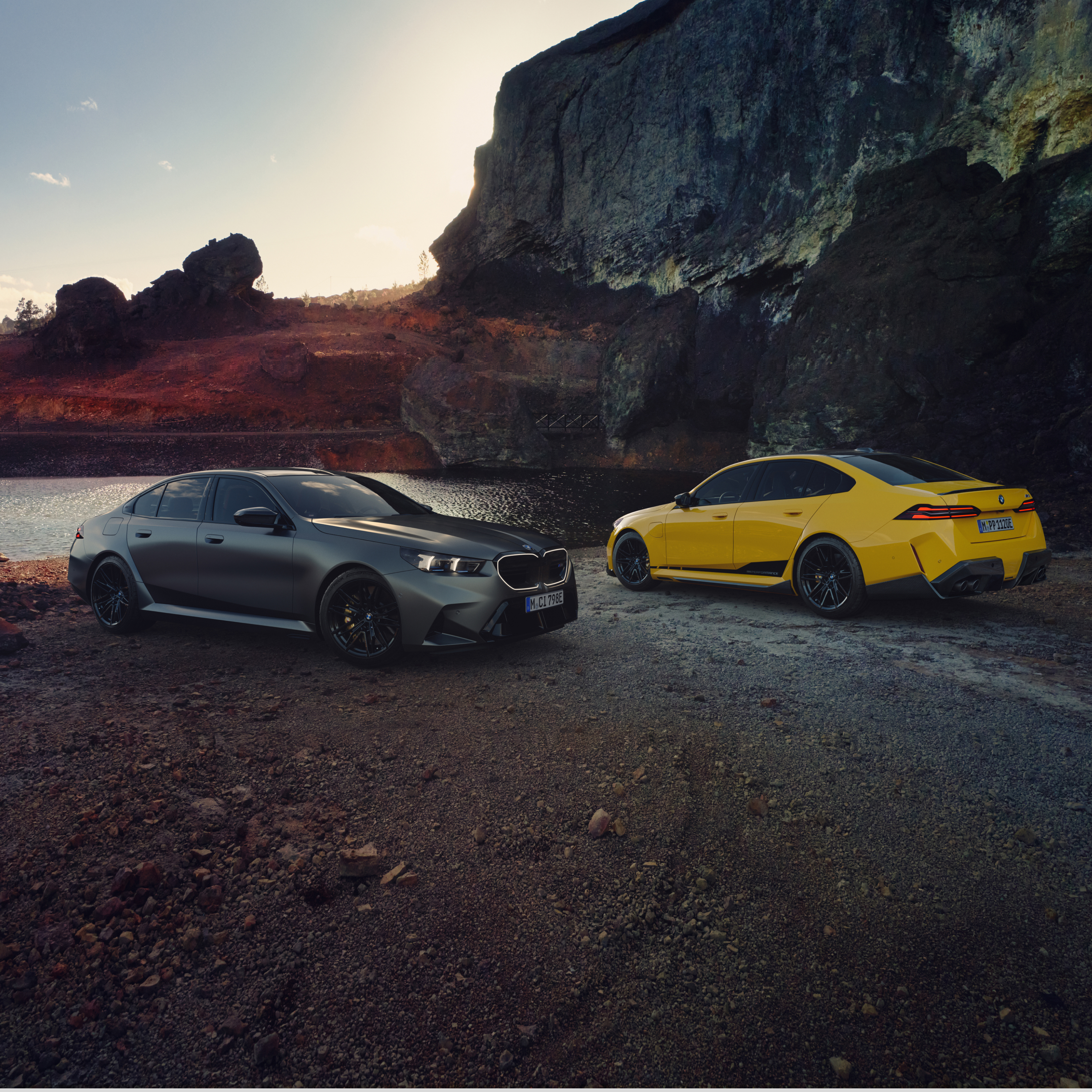 Two BMW 5 Series cars are parked on the beach in front of a rock face